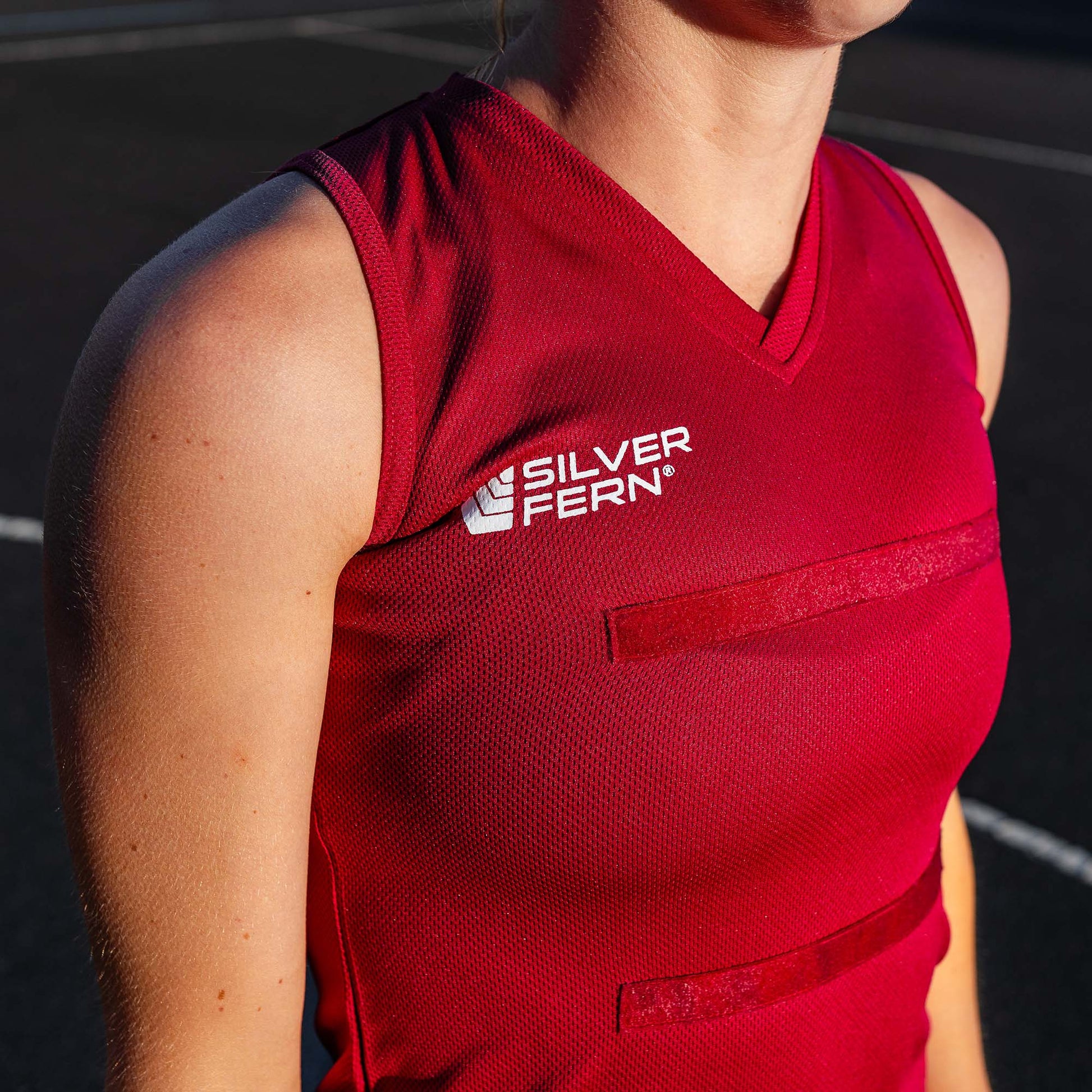 Close-up of a netball player wearing a maroon dress uniform, focusing on the upper body and the Silver Fern logo on the chest.