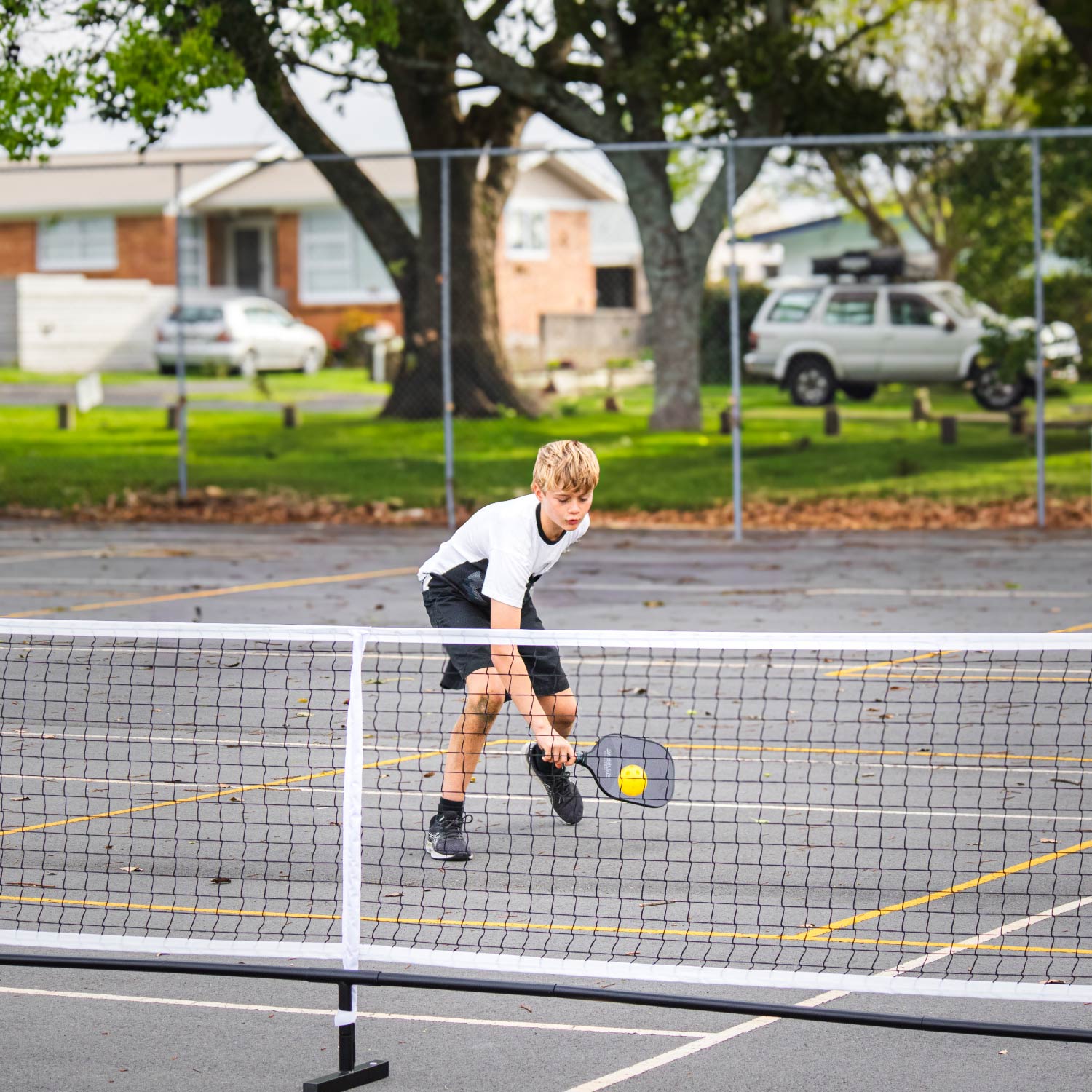 Pickleball Full Size Net Set, Action shot, kid holding a paddle and hitting the pickleball