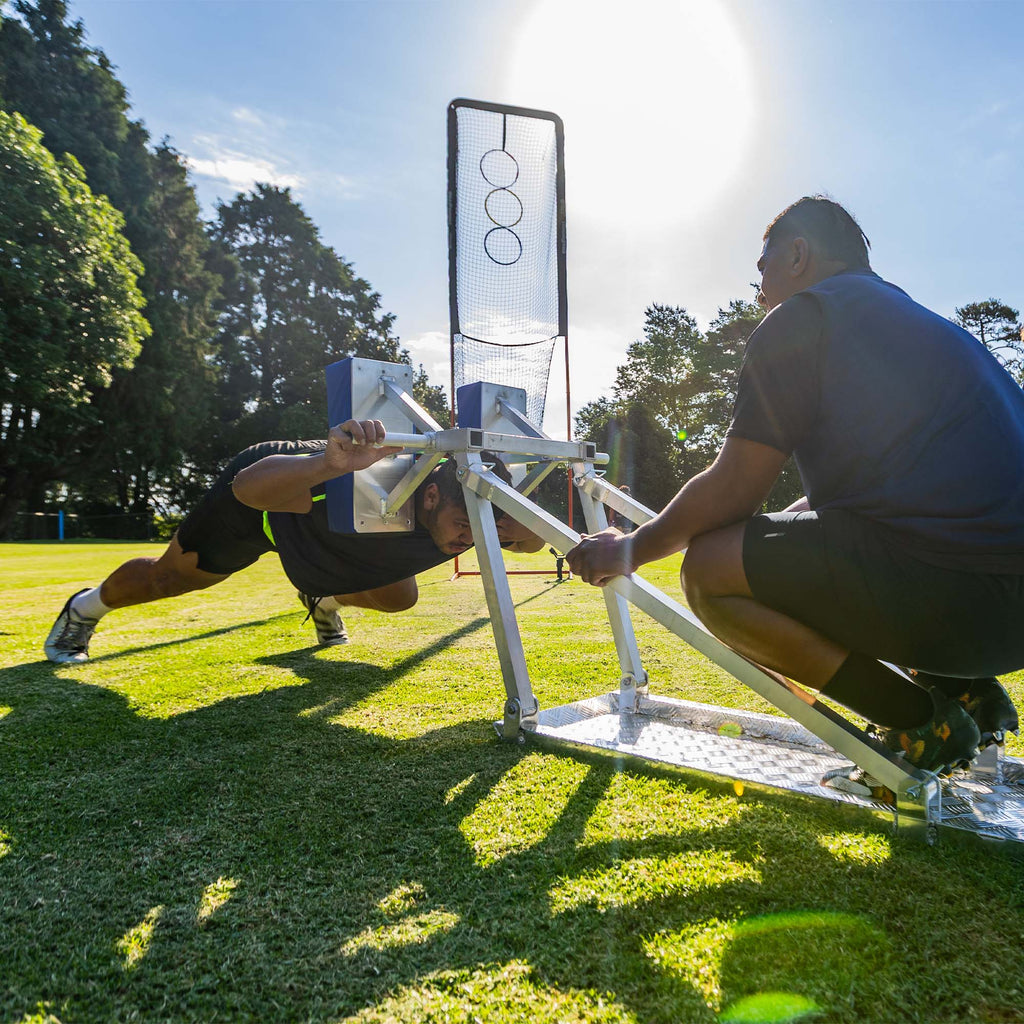 Single Player Scrum Sled in Action Lifestyle Shot of A Man Pushing the Sled with another Man weighing it down