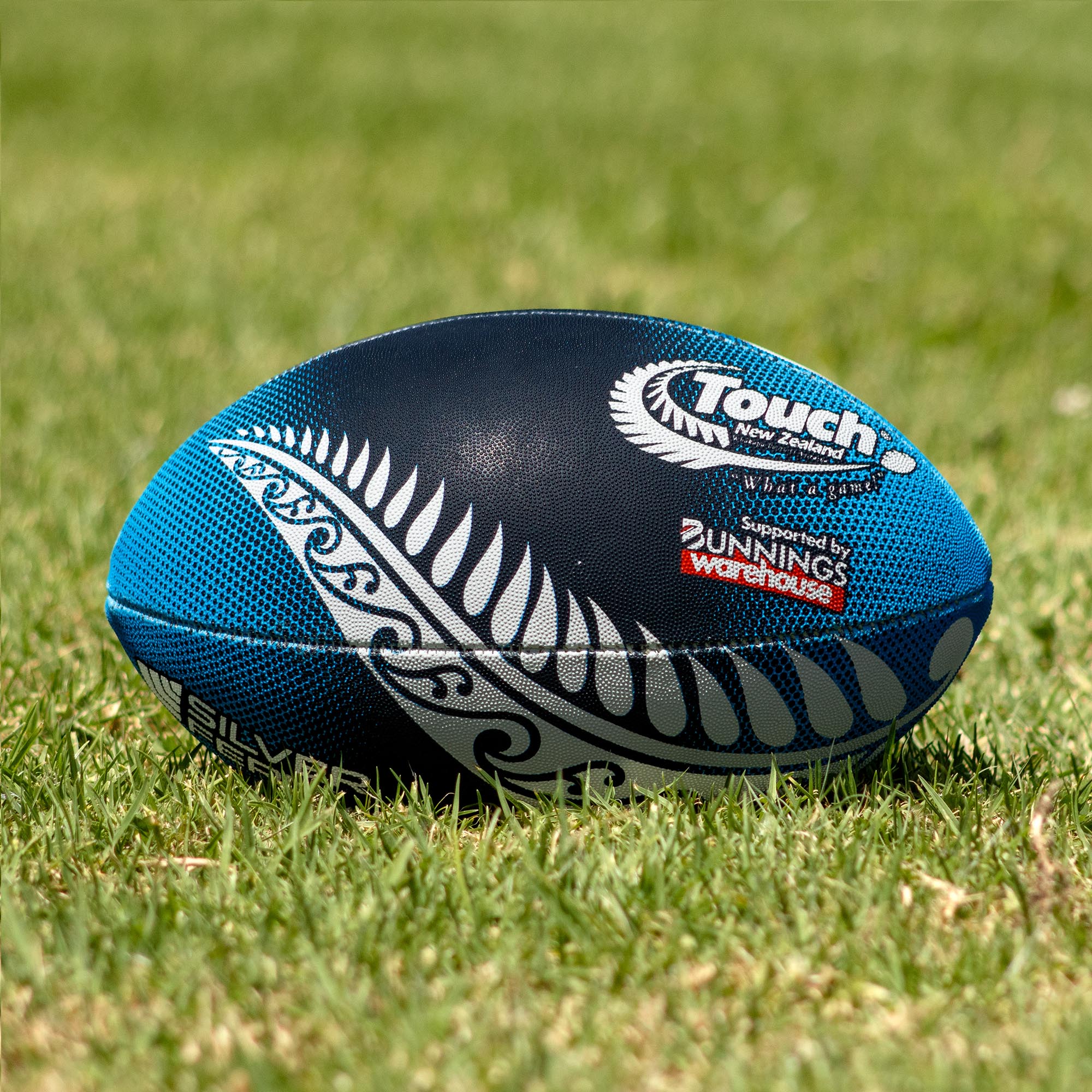 Silver Fern Touch Rugby Ball Midnight Blue Trainer, Lifestyle shot, sitting on a rugby field
